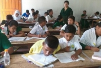 মুখে কলম কামড় দিয়ে ধরে পরীক্ষার খাতায় লিখে যাচ্ছে ছেলেটি